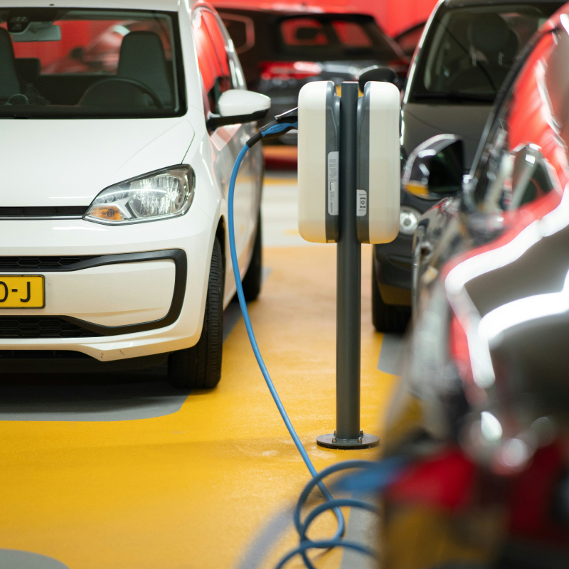 Borne de recharge double pour véhicules électriques dans un parking souterrain, avec câble bleu branché sur une voiture blanche.